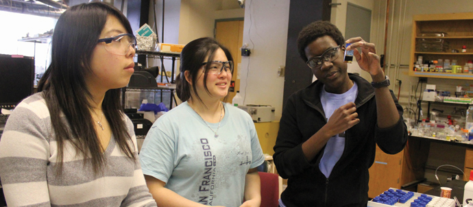 Three students in a lab examining the contents of a vial.