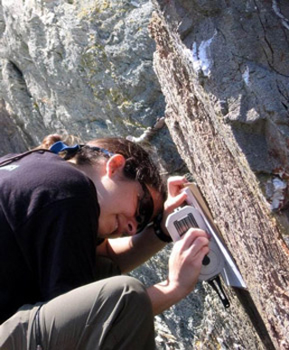 A student measuring the strike and dip of a rock face.