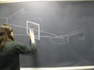 Photo of a student sketching the picture frame through which she saw the lute on the blackboard.