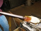 Photo of a glassblower making a vase out of the second set of white rods.