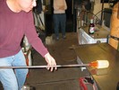 Photo of a glassblower rolling the vase on a metal table.