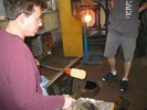 Photo of the glassblower reforming the vase with a wood paddle.