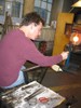 Photo of the glassblower shaping the end of the vase with a pair of tongs.