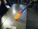Photo of a glassblower reshaping the vase on a metal table.
