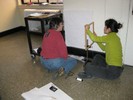 Photo of a student sitting on the floor holding up an empty wooden frame with a string passing through it.