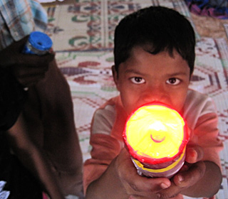 A young boy pointing a shining flashlight at the camera.