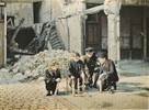 A group of four boys playing with multicolored wooden toys on a cobblestone street amidst rubble.
