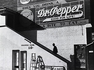 A black and white photograph showing a man walking up the steps to a movie theater with a separate entrance for African Americans.