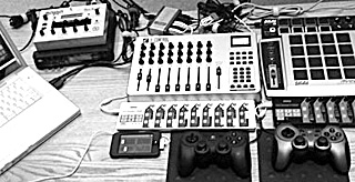 A photo of laptop computer, mixing board, iPod, two joystick controllers and several other electronic music devices arranged on a tabletop.
