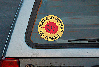 A yellow and red round sticker about anti-nuclear power is on the back window of a car. 