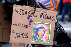 A cardboard sign held up during a protest says the seas are rising and so are the moms.