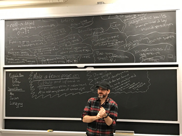 Instructor of the MIT IAP Unity course, Kyle Keane, standing in front of the chalk board during a project brainstorming session.
