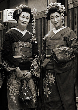 A black and white photograph of two women dressed as geishas.
