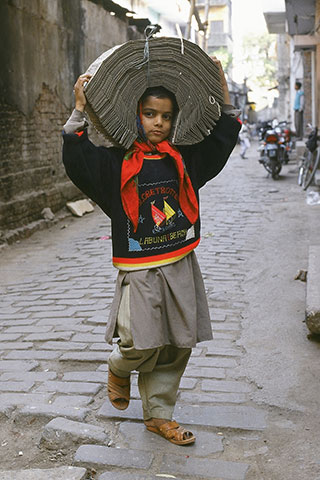 A young boy in India walks while carrying a tied up bundle of punched-data cards on his head.