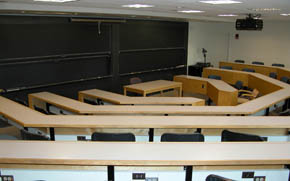 A large classroom with tiered seating, several chalkboards, and a projector.