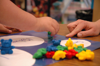 A child sorts colorful toy bears as a teacher looks on.