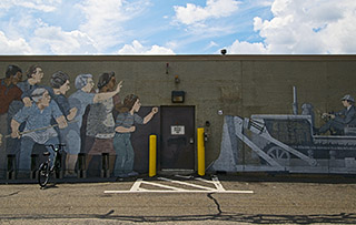 A photo of a mural depicting a group of people standing in front of a bulldozer. The bulldozer reads "Federal Inner Belt I-95".