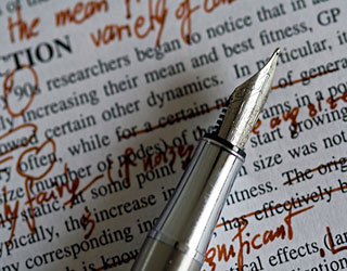 A silver fountain pen rests on top of a paper marked with edits in red ink.