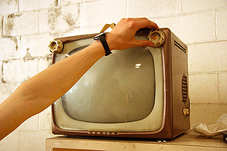 A hand turns on a small vintage television set.