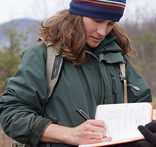A woman takes notes while standing in a field.