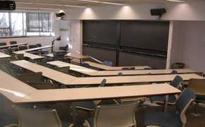 A photo taken from the back of a classroom that has five rows of seating and four blackboards.