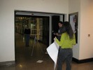 Photo of students in a hallway looking at one another through an empty wooden frame on a tripod.