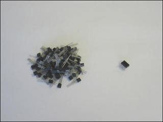 Photograph of a pile of 100 tiny discrete transistors next to an equally tiny 100 integrated transistors which are a single piece.