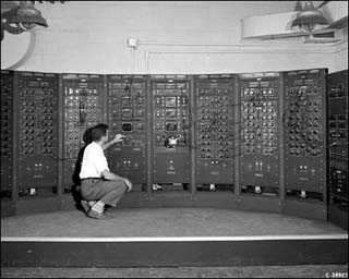A scientist squatting in front of a mainframe computer.