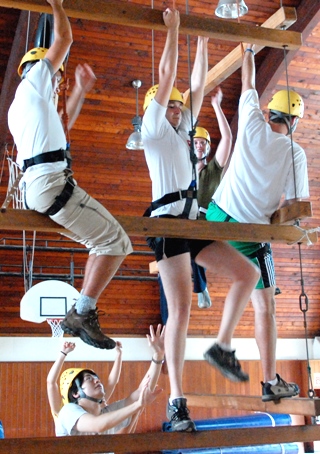 Students climbing a series of boards suspended by cables in an indoor exercise.