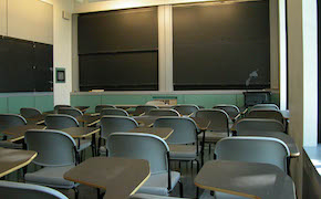 18 tablet desks arranged in rows of 6. Blackboards on the front and side walls. 