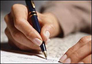 Photograph of a hand holding a pen and writing on a piece of paper.