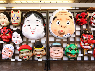 A number of Japanese masks hanging on a wall.