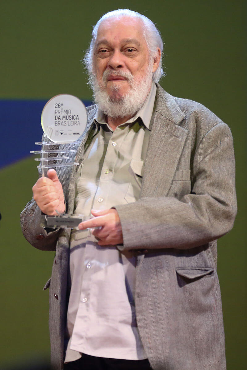 An older man holds an award on stage.