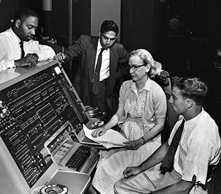 A black and white photograph circa 1960 with four people gathered around the UNIVAC I keyboard, which was the first commercial electronic computer.