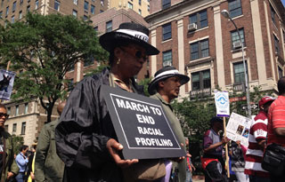 In the midst of other marchers, a black woman holds a sign reading: "March to End Racial Profiling."