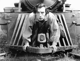 Photo of Buster Keaton crouched on the cowcatcher of a steam locomotive.