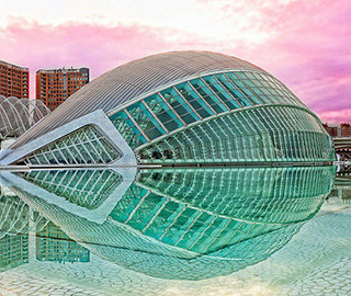 A modern structure made of glass and steel. It curves upwards into a half circle  and is reflected in the pool around it.