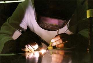 A photo of a tecnician welding, wearing a protective suit including a helmet and gloves.