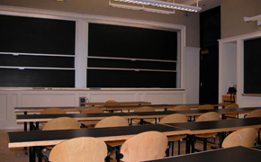 A small classroom with tables, chairs, and several chalkboards.