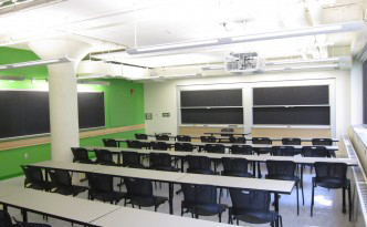 Five rows of narrow grey tables, 50 chairs, and sliding chalkboards.
