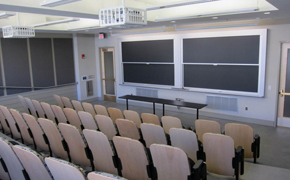 A medium-sized classroom with auditorium style seating and several blackboards.