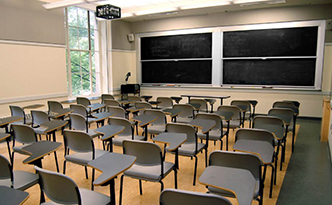 A classroom with several dozen student desks, blackboards, and a projector.