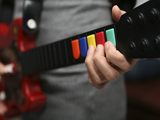A person playing a Guitar Hero controller that looks like a red electric guitar with multi-colored buttons instead of strings.