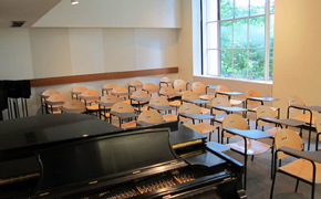 A typical classroom with rows of seats, as well as chalkboards, a projector screen, and a piano at the front of the class.
