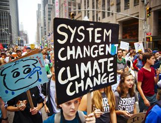 In the midst of a crowd, a young woman holds a sign with the words: System Change. Not Climate Change.