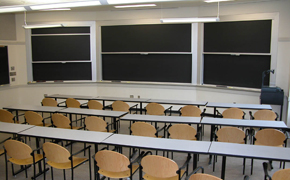 Four rows of tables and chairs are surrounded by chalkboards on all sides.