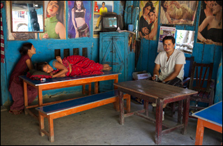 Tiwali sits across from a woman watching TV and another napping at a small colorful tea shop.