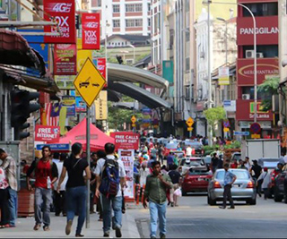 A photograph of a vibrant street scene. Shops line the sides of the road, while pedestrians walk down the middle.