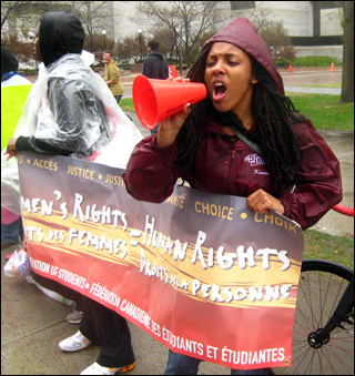 A woman shouts through a megaphone while holding a banner that says "Women's Rights=Human Rights."