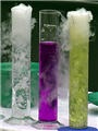 Photo of three glass cylinders containing bright liquids which appear to be bubbling and smoking.